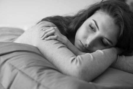 Attractive young woman lying on the bed at home, she is relaxing on a soft pillow