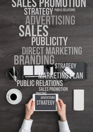 Businessman working at office desk and using a digital tablet, marketing and business text concepts coming out from the tablet's screenの写真素材