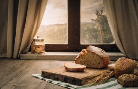 Freshly baked bread on a chopping board on the kitchen table in front of a window, healthy eating conceptの写真素材