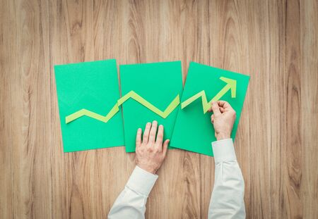 Businessman composing a successful financial chart with green arrow going up using paper cuts, financial achievement and green business conceptの写真素材