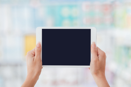 Female hands holding a digital touch screen tablet, supermarket shelves on the background, mobile app and augmented reality conceptの写真素材