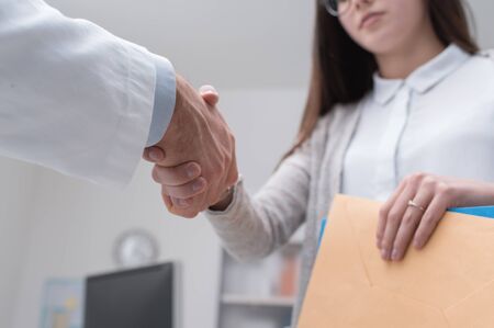Doctor shaking hands to the female patient in the office, she is holding medical records, hands close upの写真素材