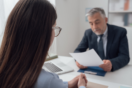 Young woman having a job interview with a corporate manager in his office, he is examining her resumeの写真素材