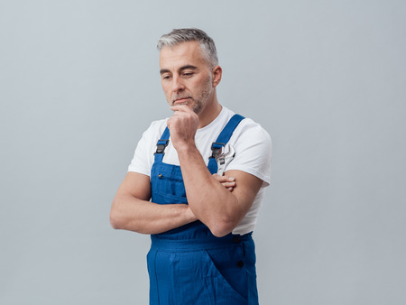 Thoughtful repairman and plumber thinking with hand on chin and holding a wrench, problems and solutions conceptの写真素材