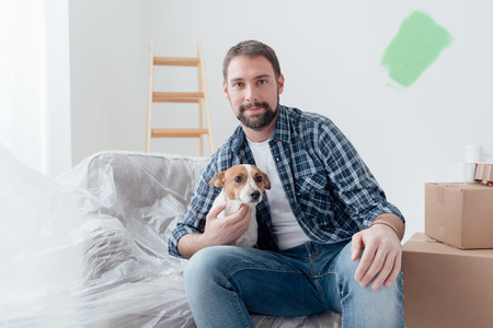 Happy dog owner posing with his pet in his new house during renovation, boxes and ladder on the backgroundの写真素材