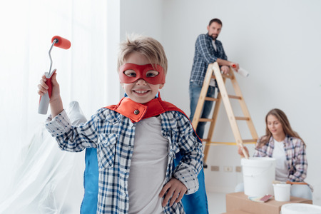 Family renovating their home and painting walls, the boy is wearing a superhero costume and holding a paint rollerの写真素材