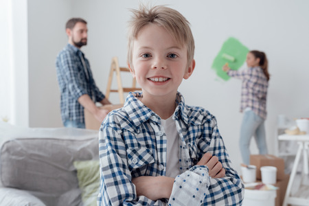 Home improvement and decoration concept: family painting a room and moving cardboard boxes, a cute confident boy is smiling on the foregroundの写真素材
