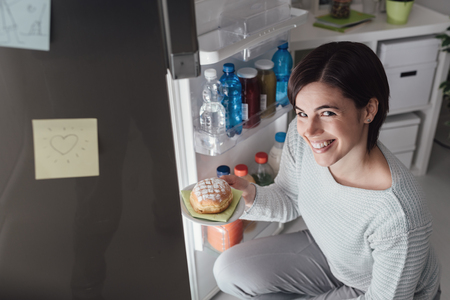 Woman having an unhealthy snack, she is taking a delicious pastry out of the fridgeの写真素材