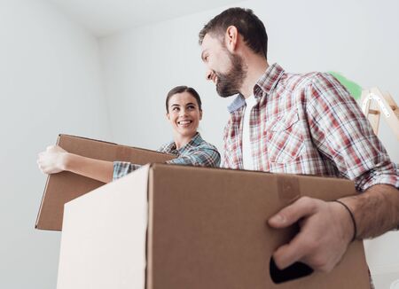 Young smiling couple moving into a new house, they are carrying full cardboard boxesの写真素材