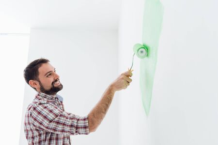 Young smiling man painting walls in his new apartment, home renovation conceptの写真素材