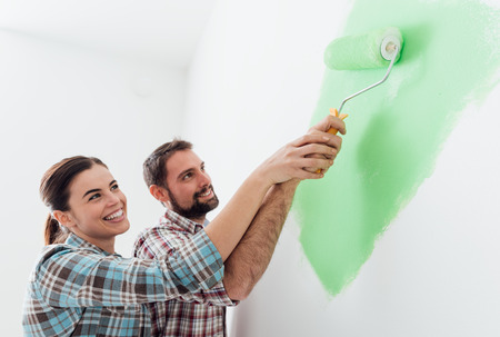 Young loving couple renovating their home, they are painting walls and holding a paint roller togetherの写真素材