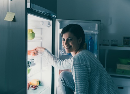 Woman in the kitchen, she is taking food out of the fridge and smiling at cameraの写真素材