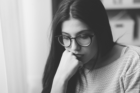 Unhappy woman with glasses posing with hand on chin, she is depressed and looking downの写真素材