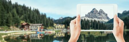 Tourist exploring the Dolomite mountains and taking a picture with a touch screen tablet, travel and nature conceptの写真素材