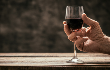 Senior wine expert tasting a glass of red wine in the cellar, hand close up, wine tradition and culture conceptの写真素材
