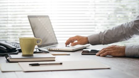 Businessman working at office desk, he is using apps on a digital tablet and connecting with a laptopの写真素材
