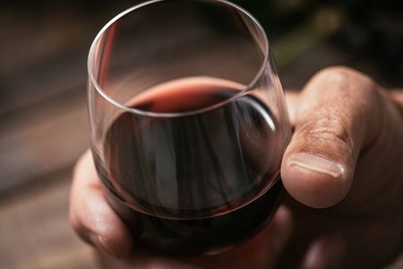 Senior man tasting a glass of italian red wine, rustic wooden table on the background, hand close upの写真素材