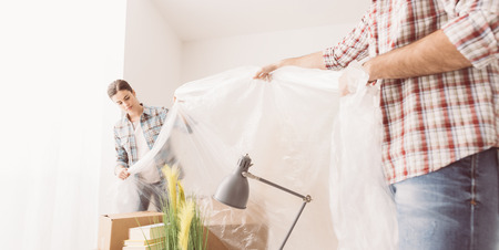 Two people preparing a room for painting, they are covering boxes and objects with a protective plastic sheet, home renovation conceptの写真素材