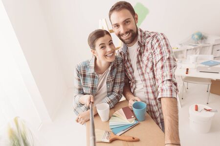 Smiling young couple moving into their new house and doing a home makeover, they are taking a selfieの写真素材