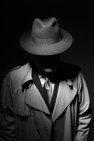 Man posing in the dark with a fedora hat and a trench coat, 1950s noir film style characterの写真素材