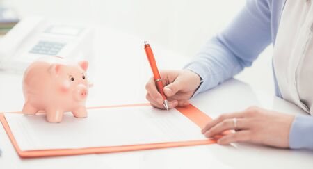 Woman signing a contract and piggy bank: financial planning, loan financing and insurance conceptの写真素材