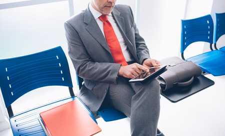 Corporate businessman sitting in the waiting room and connecting with a digital touch screen tablet, he is waiting for a meetingの写真素材