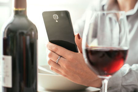 Woman using a wine app at the restaurant, she is scanning a wine label on a bottle, wine tasting and technology conceptの写真素材