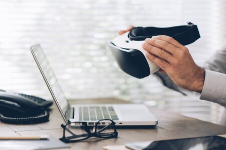 Corporate businessman working at office desk and holding a virtual reality headset: business and innovative technology conceptの写真素材