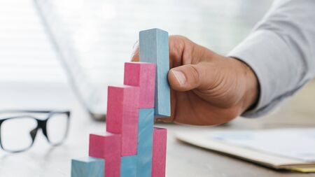 Businessman working at office desk, he is building a growing financial graph using wooden toy blocks: successful business conceptの写真素材