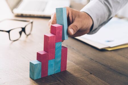 Businessman working at office desk, he is building a growing financial graph using wooden toy...