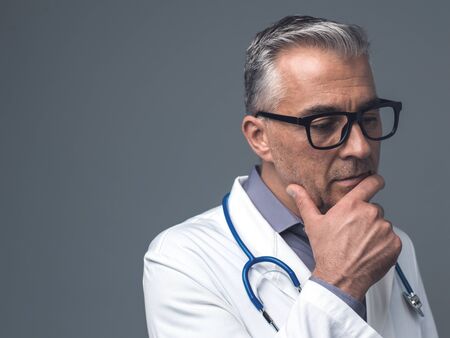 Chief physician thinking with hand on chin: medical advice, diagnosis and healthcare professionals conceptの写真素材