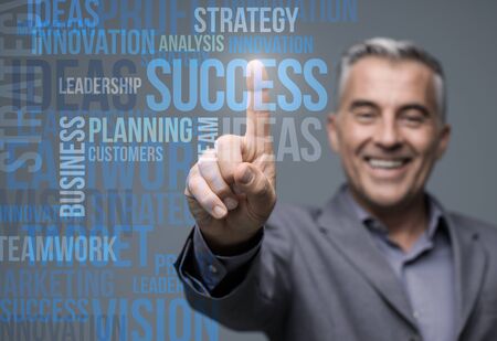 Successful smiling businessman using a virtual touch screen interface and selecting business conceptsの写真素材