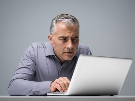 Mature businessman working with a laptop and having vision problems, he is staring closely at the computer screenの写真素材