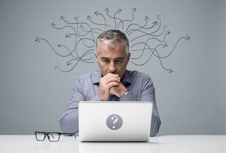 Focused businessman sitting at desk and working with a laptop, he is thinking about business...