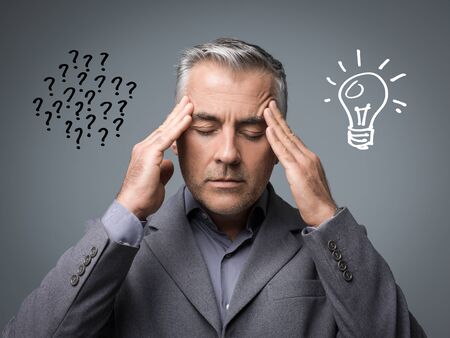 Businessman solving problems and thinking about strategies, he has question marks on the left and a lit bulb on the rightの写真素材