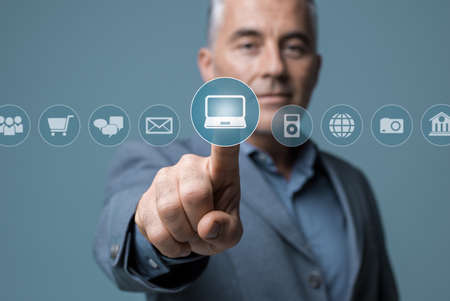 Businessman using a visual interactive interface with icons, he is selecting apps on a virtual dashboardの写真素材