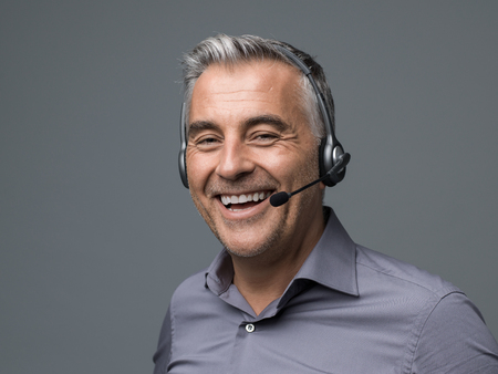 Cheerful customer support phone operator with headset, he is talking with a customer and smilingの写真素材