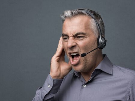 Angry aggressive customer support phone operator with headset, he is yelling and having a dicussion with a customerの写真素材