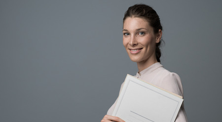 Professional female secretary holding paperwork and smiling at cameraの写真素材