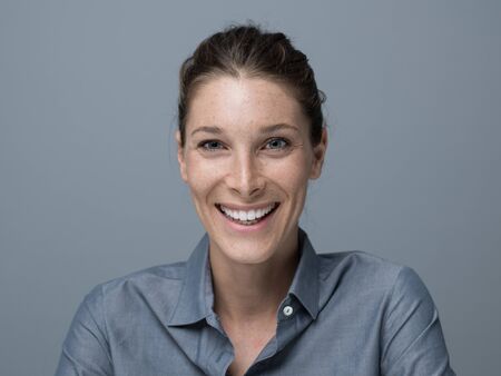 Confident cheerful young woman posing on gray background, she is smiling at cameraの写真素材