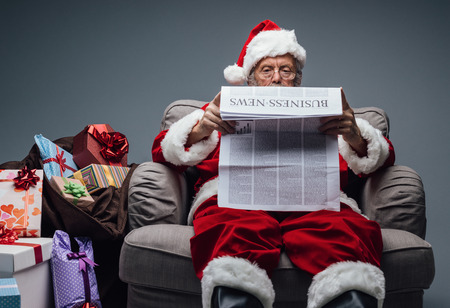Santa Claus reading business news on a newspaper and relaxing on the armchair at homeの写真素材