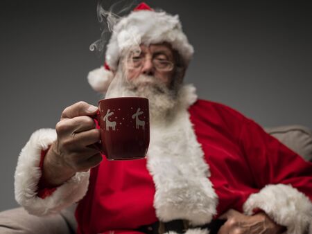 Santa Claus relaxing at home on the armchair and having an hot drinkの写真素材