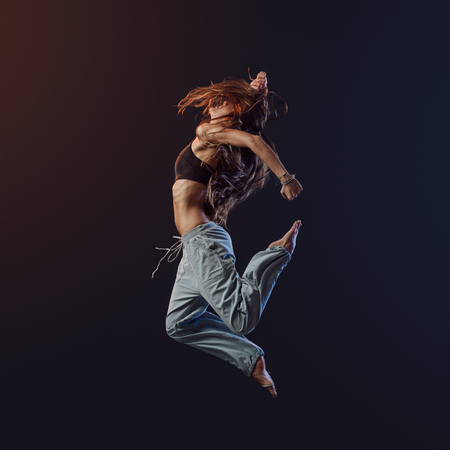 Young athletic slim dancer performing and jumping on dark background, fitness and vitality conceptの写真素材