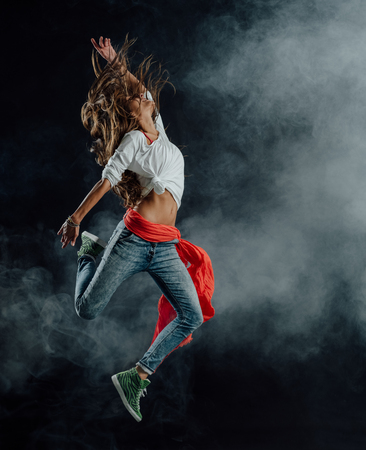 Female modern style performer dancing on dark background, she is dancing with a scarf tied around her waistの写真素材