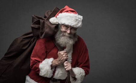 Smiling Santa Claus carrying a sack with gifts on Christmas Eveの写真素材