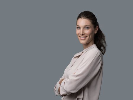 Smiling young woman wearing an elegant shirt and posing with arms crossed, she is smiling at cameraの写真素材