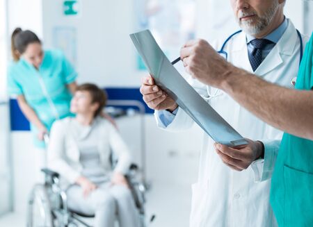 Confident professional doctors examining a patient's x-ray and woman on wheelchair helped by a nurse...