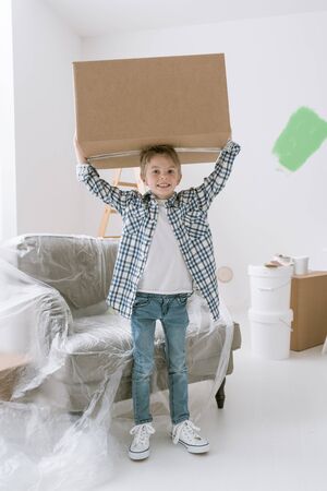 Smiling boy carrying a huge box, home renovation and relocation conceptの写真素材