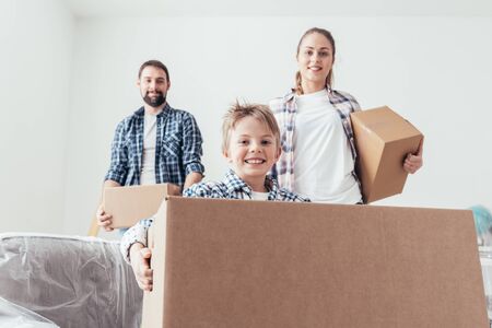 Young family relocating and renovating their new house, they are carrying boxes, boy smiling on the foregroundの写真素材