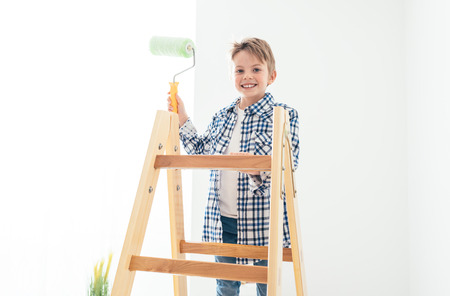 Cute smiling boy standing on a ladder and holding a paint roller, home renovation and decoration conceptの写真素材